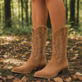 Tan embroidered western boots worn on a leaf-covered forest trail