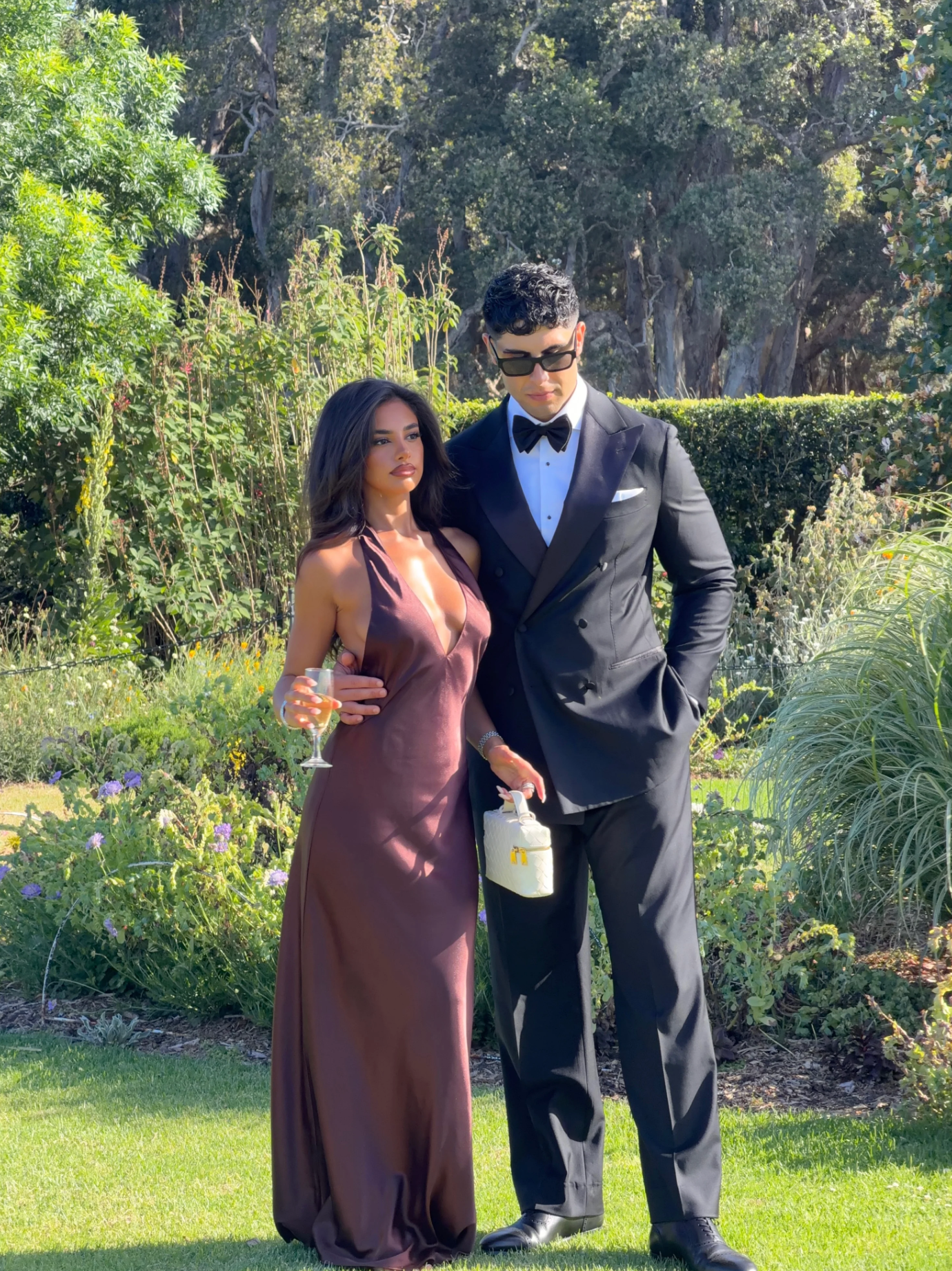 Brown satin halter maxi dress worn as wedding guest attire in a garden