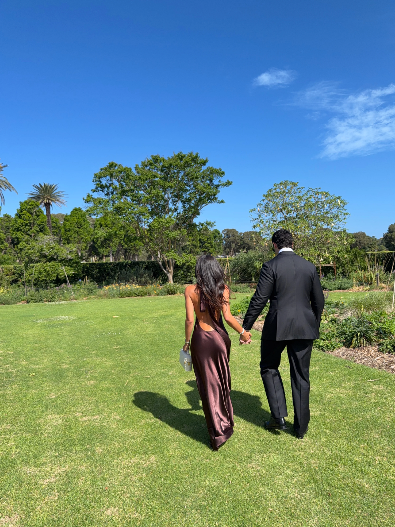 Brown satin halter maxi dress, back view walking through a garden