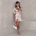 Multicolour print mini dress with puff sleeves, worn against a wall