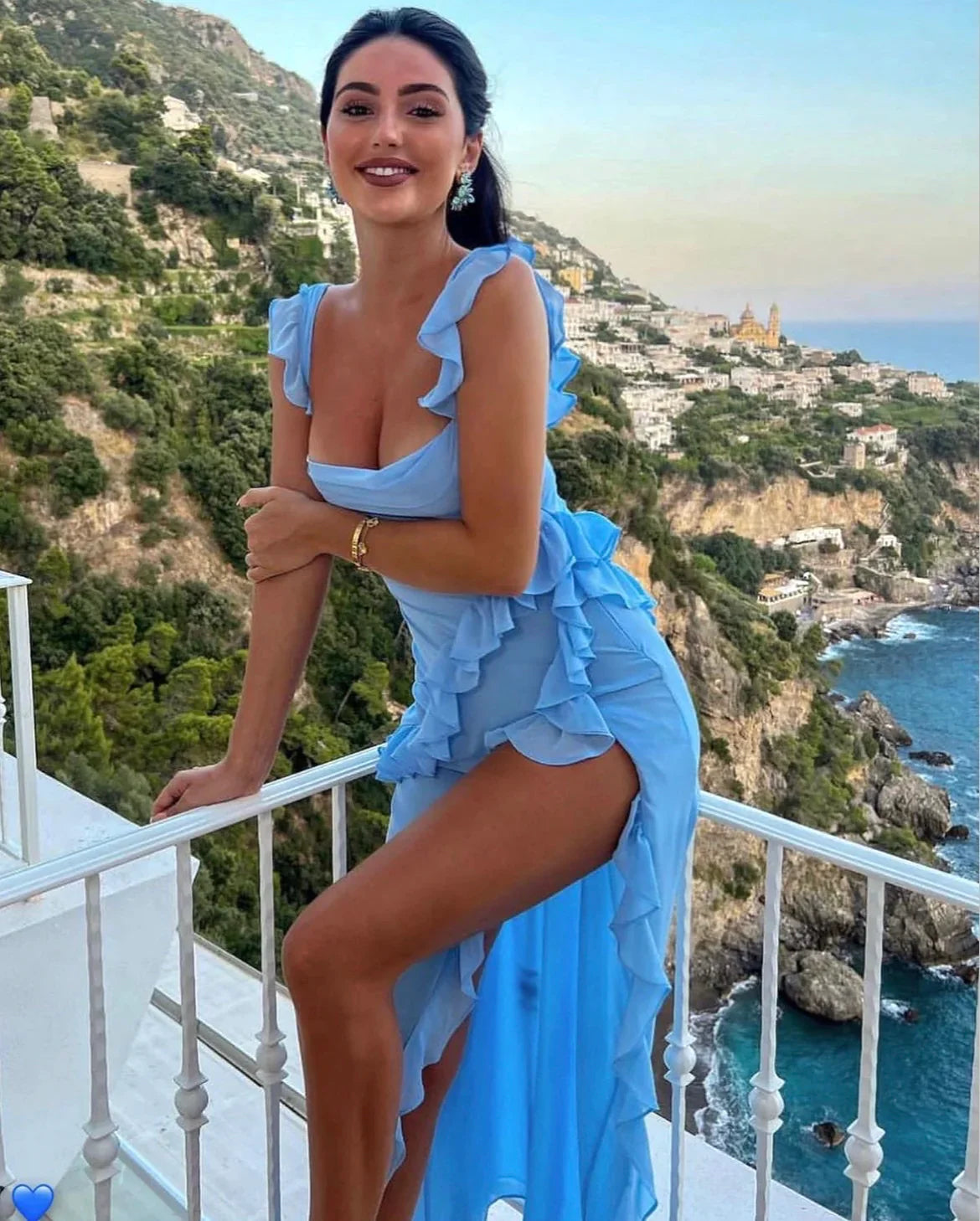 Blue ruffled maxi dress with a front slit worn on a coastal balcony