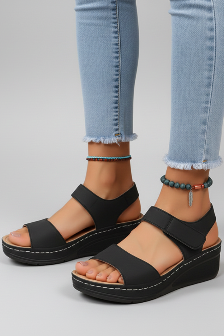 Black open-toe wedge sandals worn with denim, front view